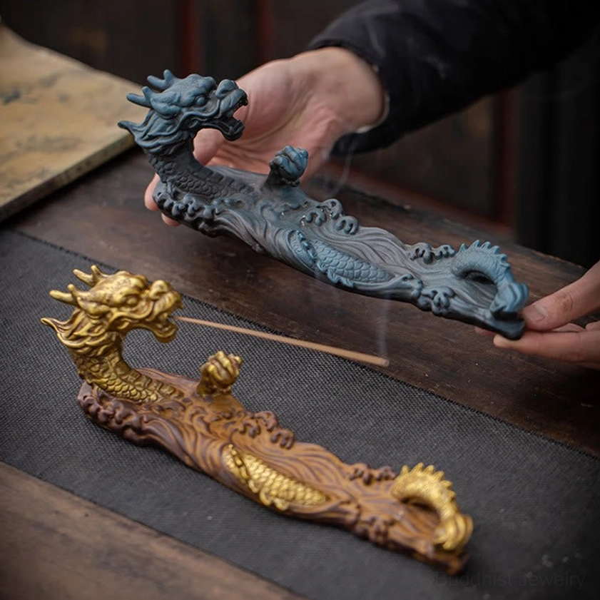 Blue brown and gold dragon ceramic incense holders displayed together on wooden table, hands holding blue incense burner