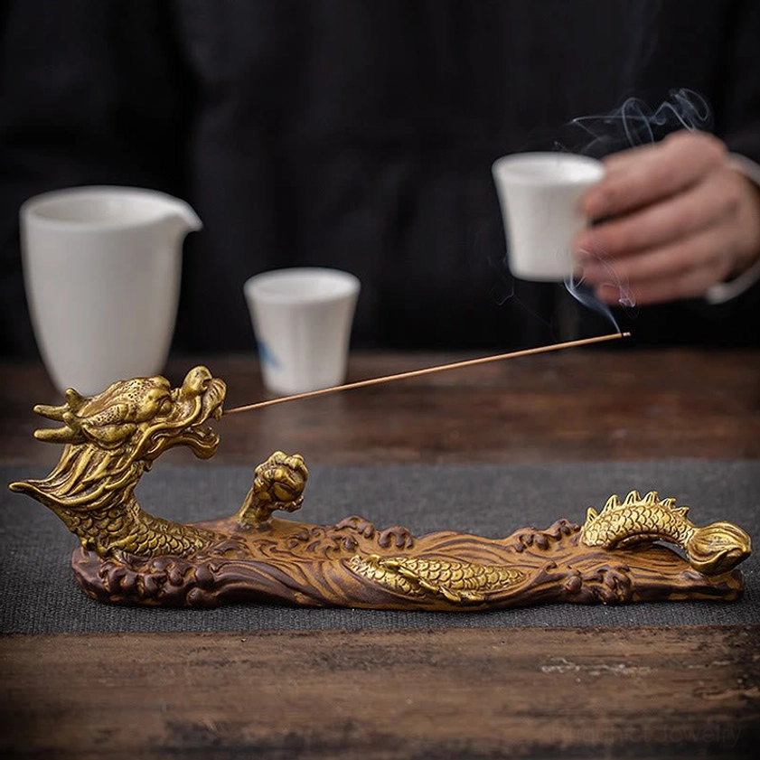 Flat lay display of dragon incense burner with burning incense on wooden tea table surrounded by tea wares