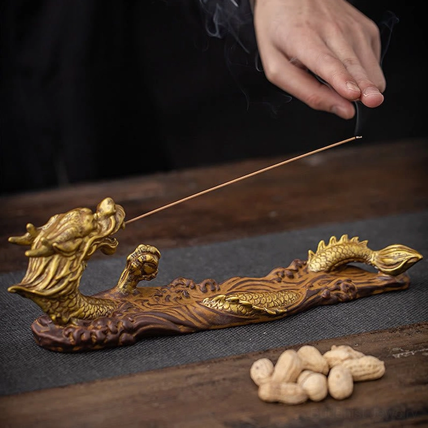 High side view of golden dragon incense burner with hand lighting the incense stick on wooden tea table