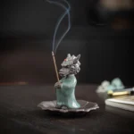 Dragon King ceramic incense burner with celadon glaze and ruby jewel on lotus tray, front left oblique view showing burning incense