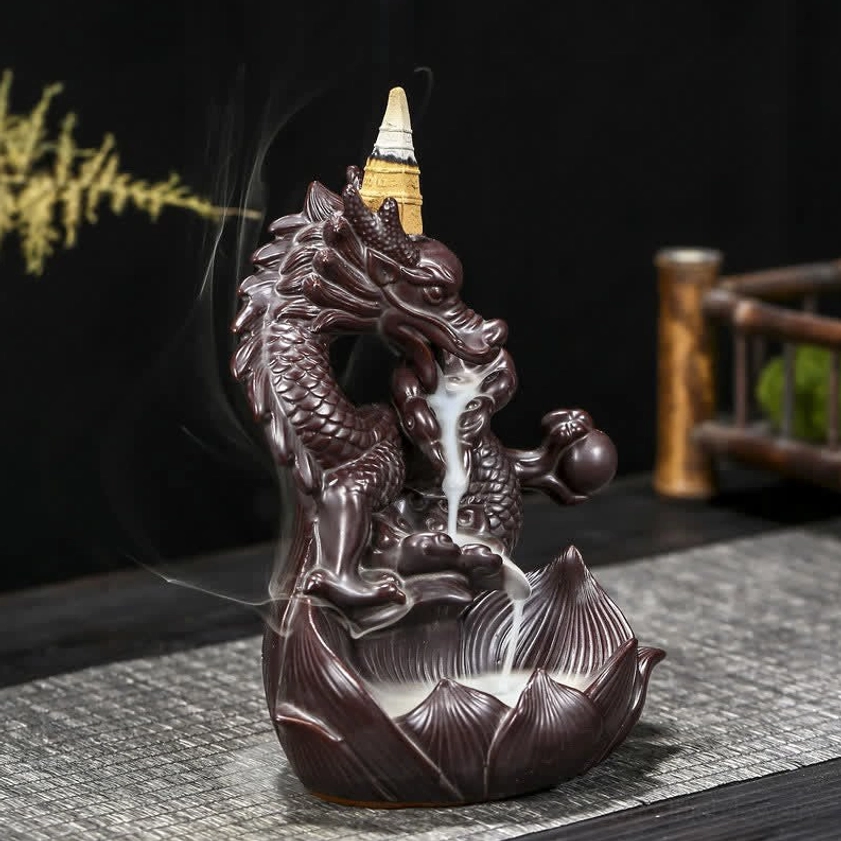 Dark brown ceramic backflow incense burner showing detailed dragon carving and visible smoke stream, left side view with green decorative elements