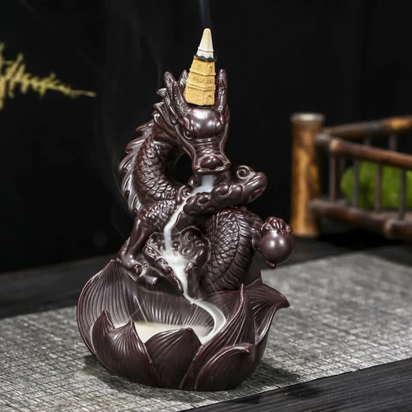 Hand-sculpted ceramic incense burner featuring dragon holding sacred sphere ornament, right front three-quarter view with backflow smoke on wooden table