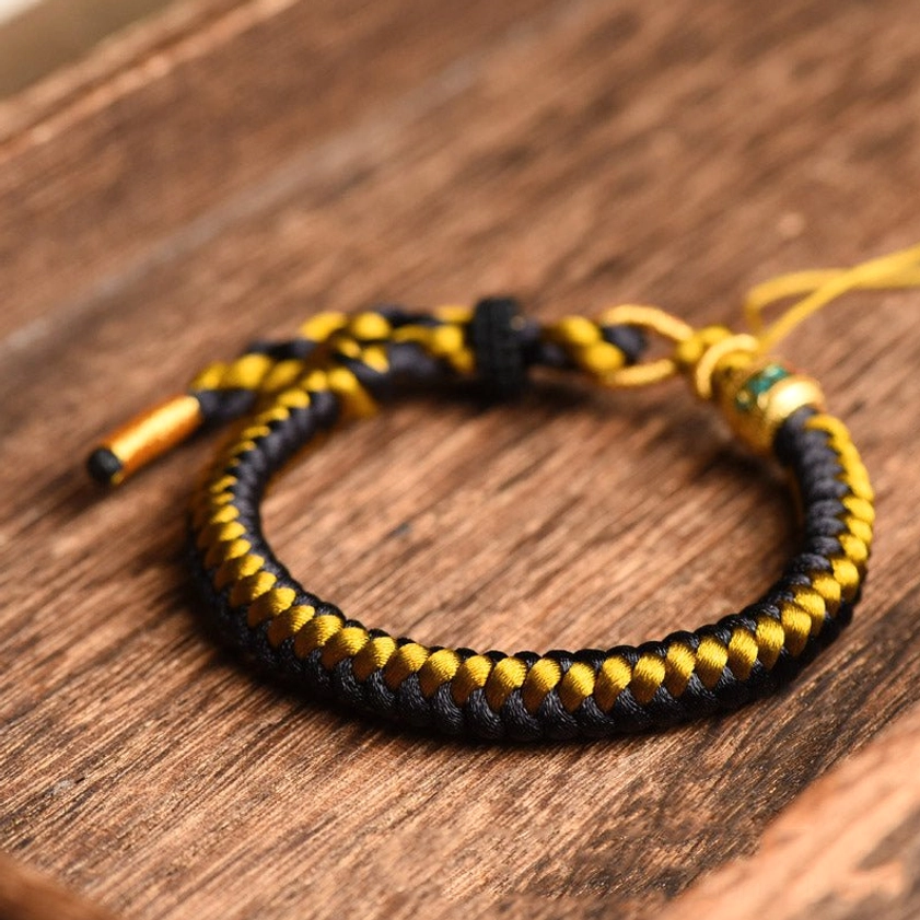 Close-up side view of black and gold twisted rope Om Mani Padme Hum bracelet showing dragon scale texture detail