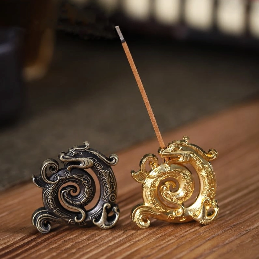Dragon incense holder close-up showing intricate carved patterns with incense stick inserted, eye-level view on light wooden table