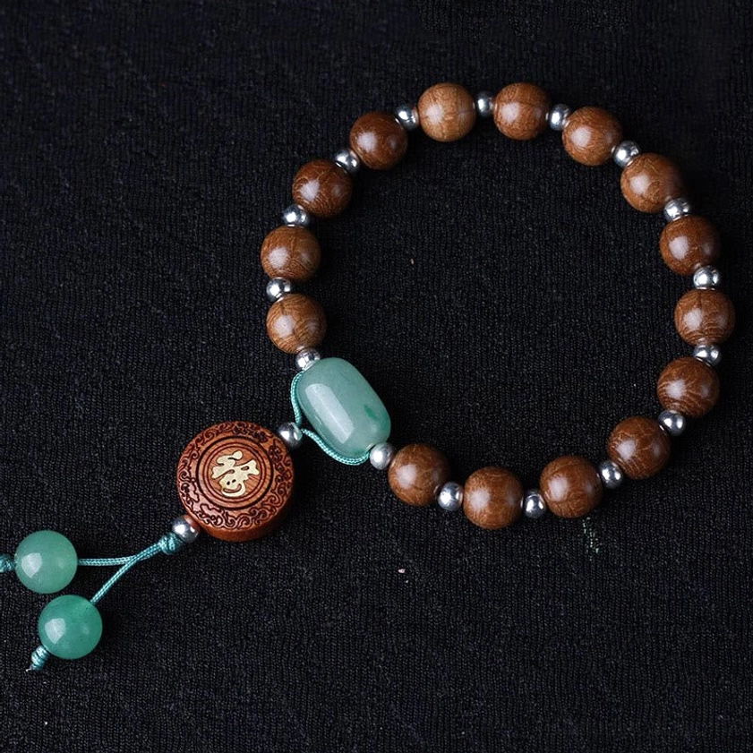 Circular arrangement of dragon wood Buddhist blessed bracelet with 15 beads, Om Mani Padme Hum pattern, and dual jade tassels on black background