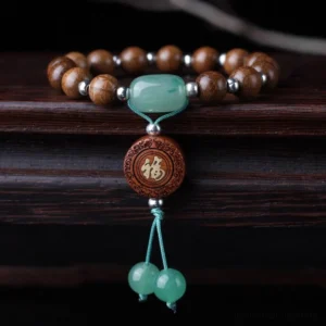 Abelia Biflora dragon wood Buddhist bracelet with 15 beads, green jade, Fu charm, and decorative tassel on dark wooden surface - top-down flat lay view