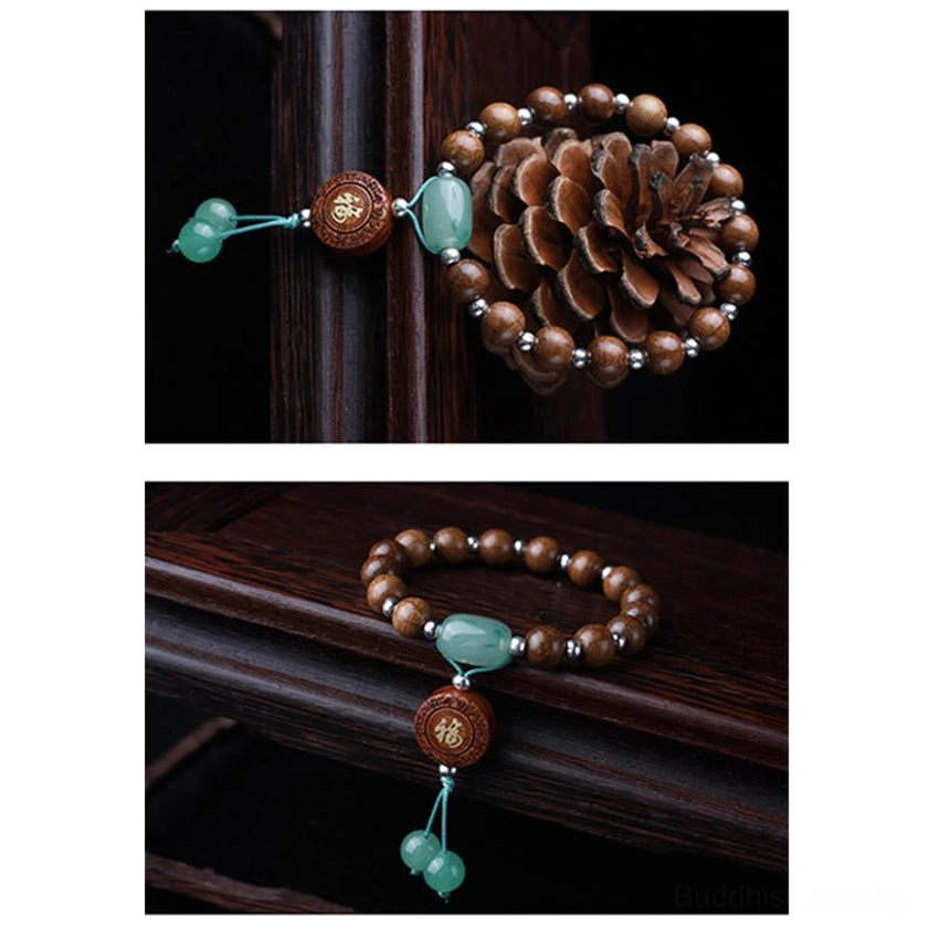 Dragon wood Buddhist meditation bracelet displayed on wooden table beside pine cone, featuring brown om mani padme hum beads and jade tassel