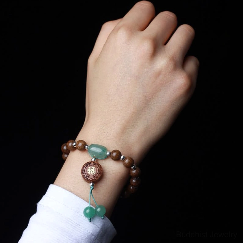 Worn on wrist close-up of dragon wood Buddhist meditation bracelet with brown beads, jade accent, and spiritual Fu charm - hand detail shot