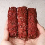 Dragons Blood Sage Smudge Stick bundle held in two palms, showing deep red dried herbs wrapped with natural twine for energy cleansing