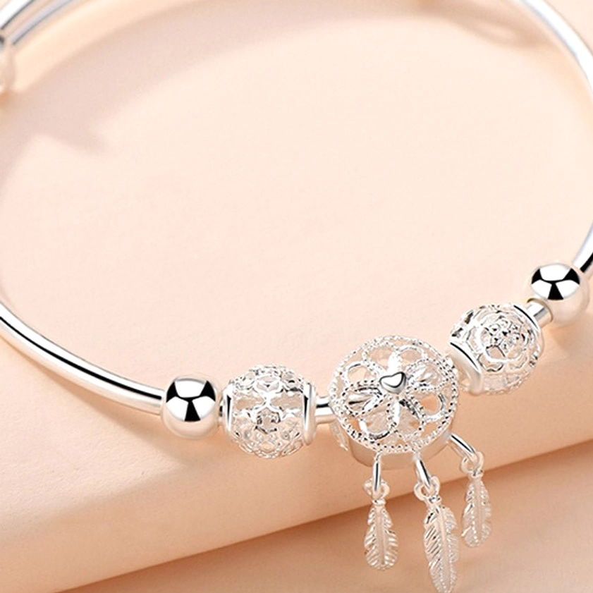 Close-up top view of open bangle dream catcher buddhist blessing bracelet showing clear hollow carvings and shiny silver metal feather tassels