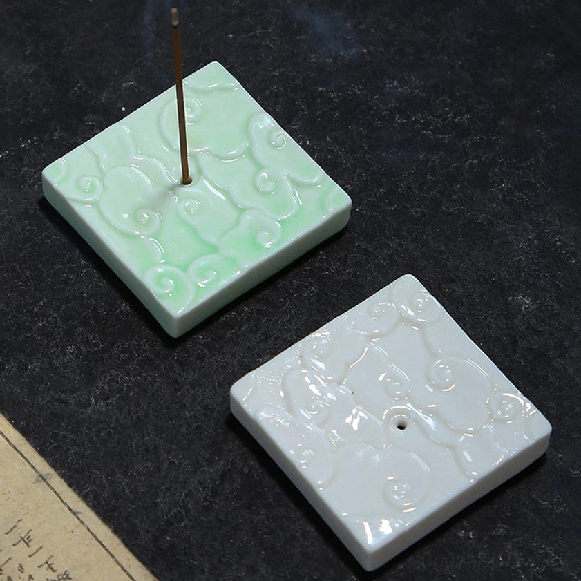 Top-down flat lay of white and celadon green ceramic cloud incense holders on dark stone surface with aged paper detail, showcasing both color variants and design craftsmanship
