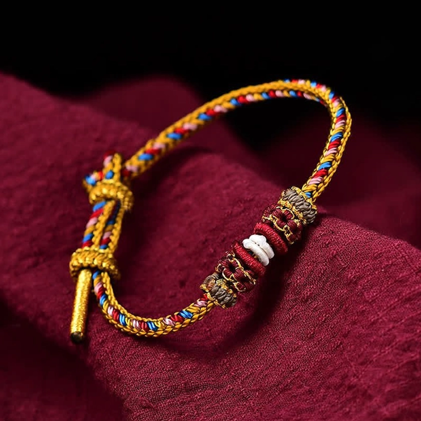 Handmade Dunhuang lucky braided string bracelet multicolor woven design with decorative knots displayed on dark red fabric