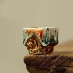 Dunhuang meditating Buddha Shino ceramic teacup with flowing multicolor glaze and gilded seated Buddha relief on aged wooden surface, low side view