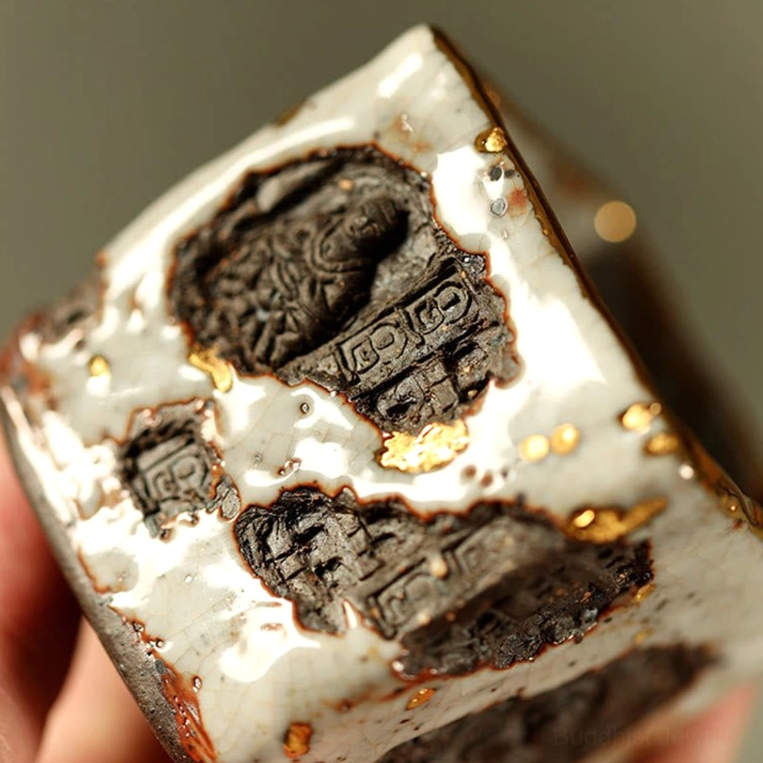 Handcrafted Shino ceramic tea cup held at oblique angle showing multiple carved grotto motifs and gold splatter accents with aged glaze