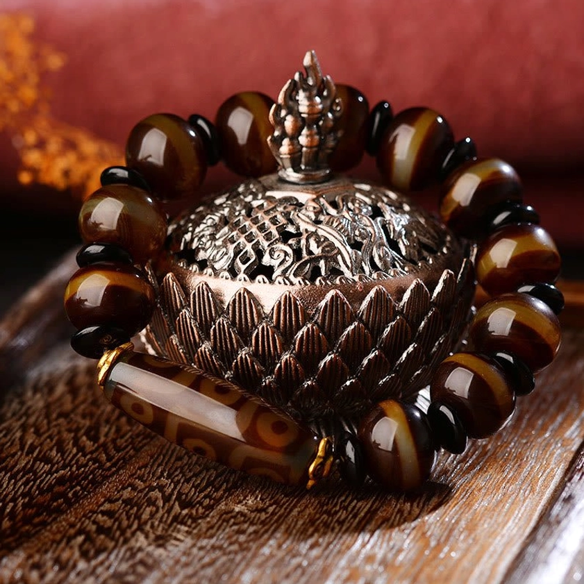 Nine-eye dzi agate bracelet three-quarter view showing warm brown striped agate beads and central dzi bead on textured mat