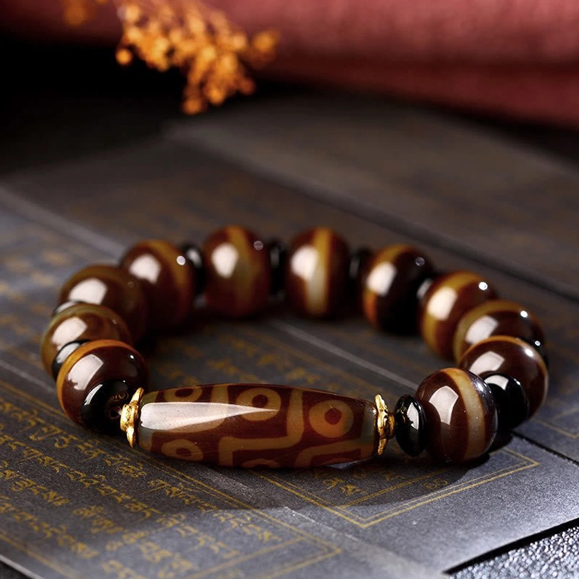 Buddhist nine-eye dzi agate bracelet overhead view with patterned dzi bead center and gold tone hardware on vintage text background