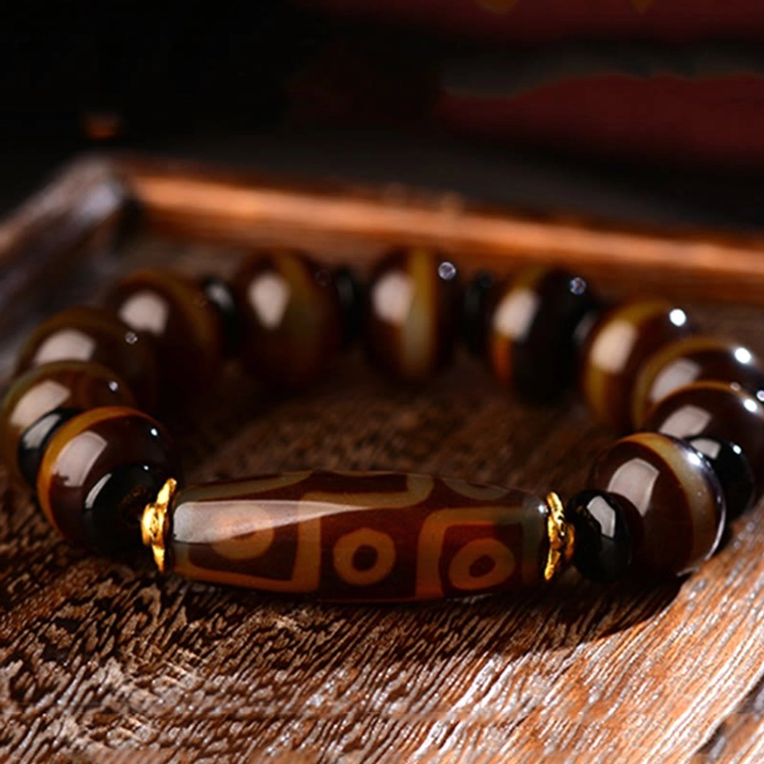 Nine-eye dzi agate bracelet overhead view with rich brown striped agate beads and gold tone hardware on natural wood background