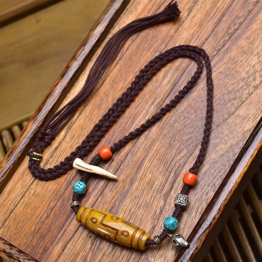 Buddhist dzi bead bone pendant necklace with orange and turquoise beads, braided rope design, and silver metal fittings on wooden surface