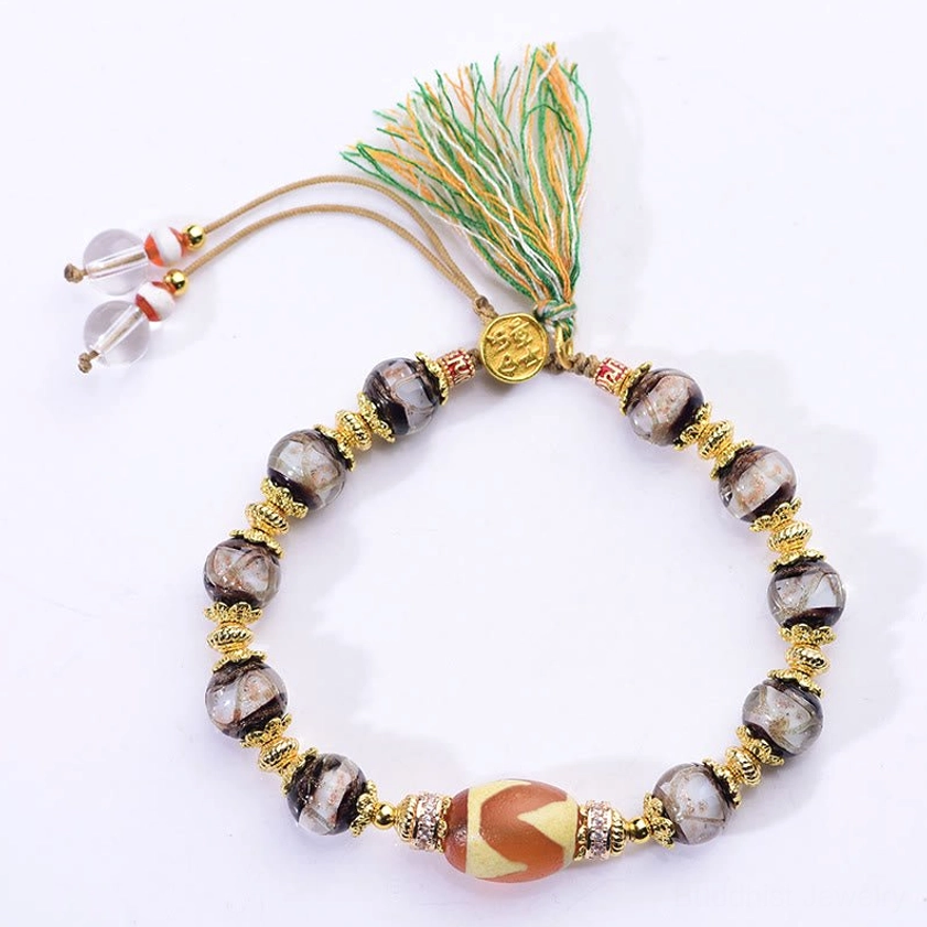 Sacred nine-eye dzi bead center stone with tassel closure and clear crystal accents on light tabletop
