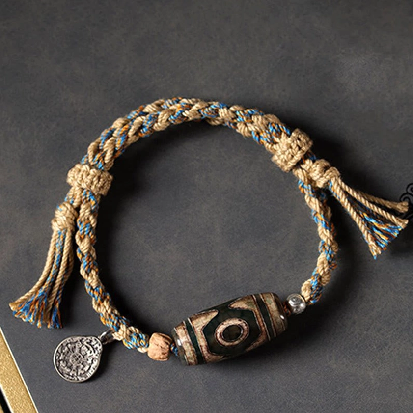 Mixed color braided dzi bead bracelet with vintage stone bead and silver charm on dark surface