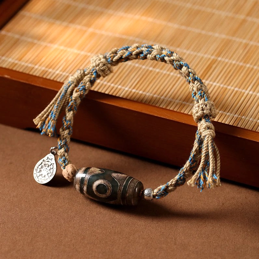 Nine-eyed dzi bead bracelet with dark brown bead and silvered metal spacer on wooden background