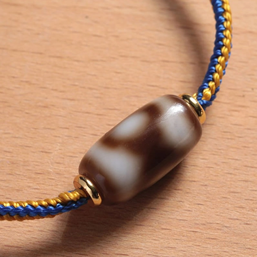 Detailed macro side flat lay of three-eye Dzi bead bracelet showing brown-white stone pattern and gold accents