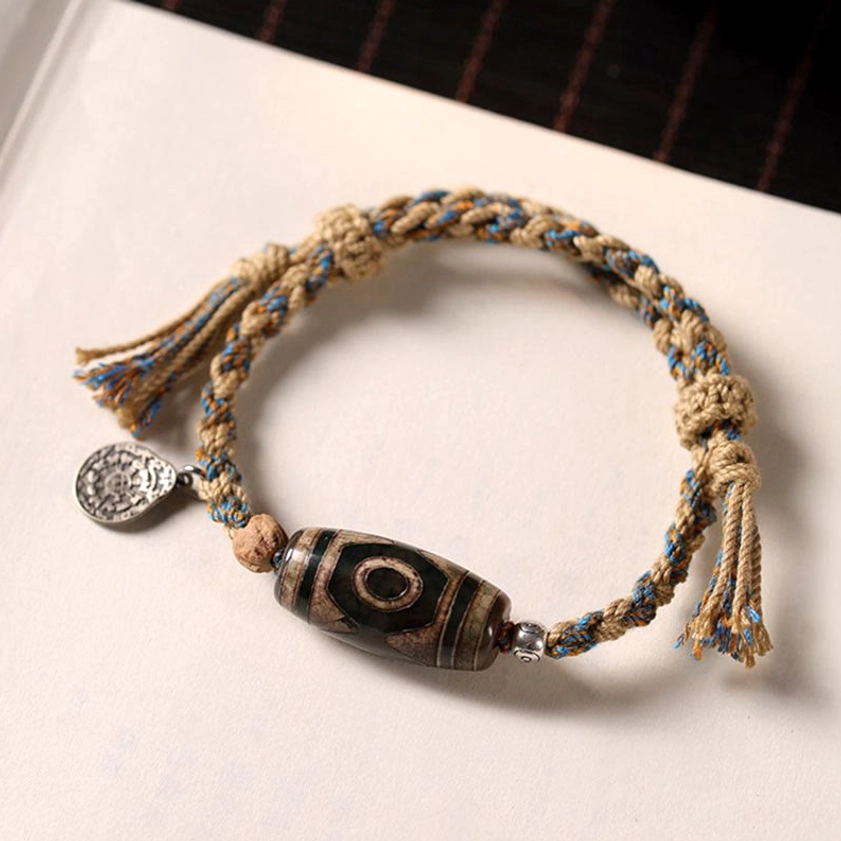 Authentic dzi bead protection bracelet with aged metal charm and tassel details on white surface