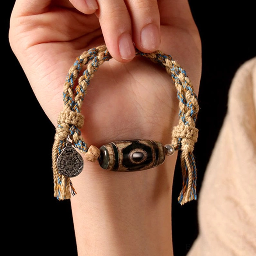 Nine-eye dzi bead string bracelet in hand showing mixed color braided rope and round metal pendant