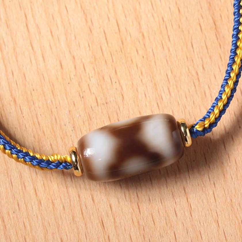 Macro close-up of three-eye Dzi bead pattern and gold metal rings on wooden table