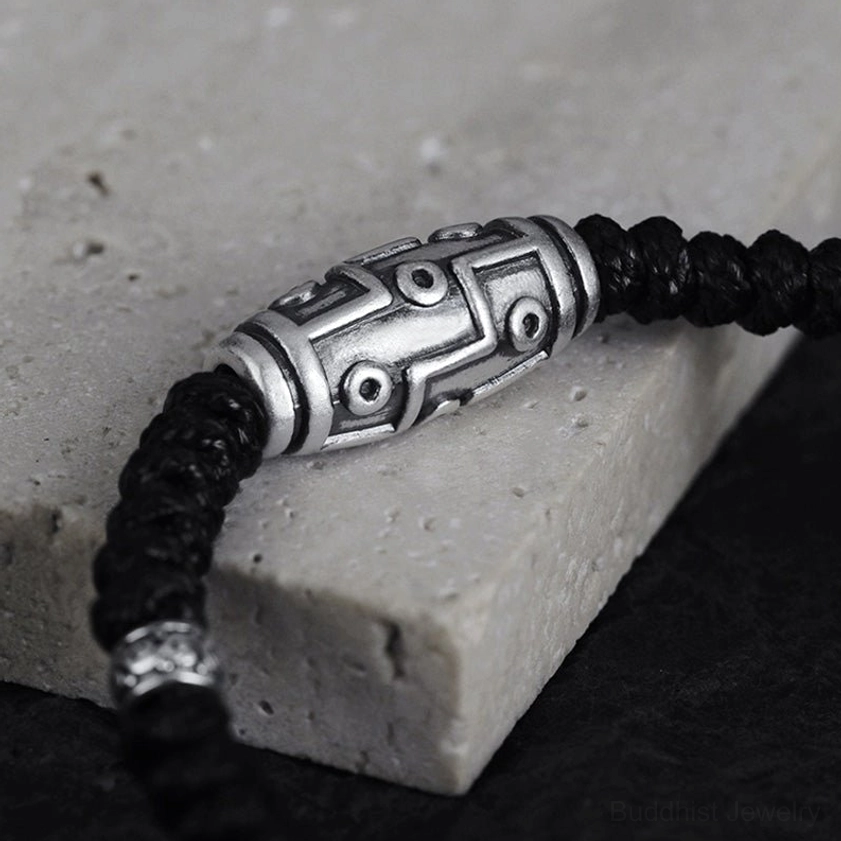 Low angle side view of 999 sterling silver dzi bead bracelet on stone surface, showing silver spacer beads and woven cord