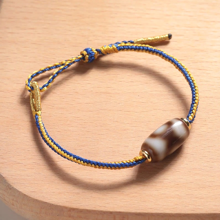 Three-eye Dzi bead bracelet overhead side view showing dual-tone woven rope and gold metal accents on wooden coaster