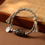 Nine-eye Dzi bead bracelet with brown and blue twisted braided rope displayed on bamboo tray, showing authentic handmade Buddhist jewelry