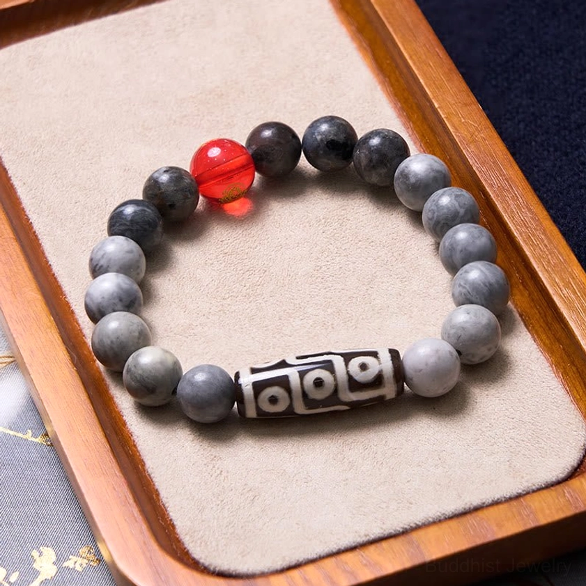 Buddhist nine-eye dzi bead bracelet on wooden tray with velvet pad showing gray matte beads and black-white dzi charm