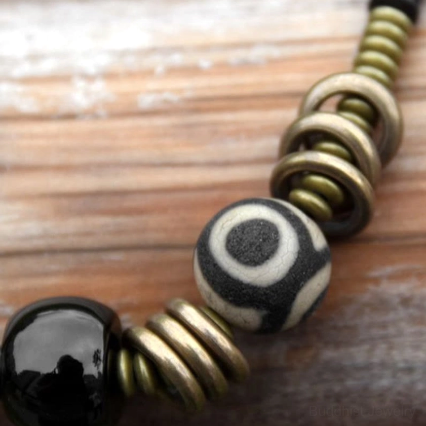 Close-up detail of dzi bead bronze metal rings and black onyx stone on wooden surface