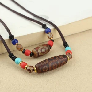 Dzi bead Buddhist necklace flat lay top view showing nine-eye and three-eye pendant with colorful agate spacer beads on braided cord