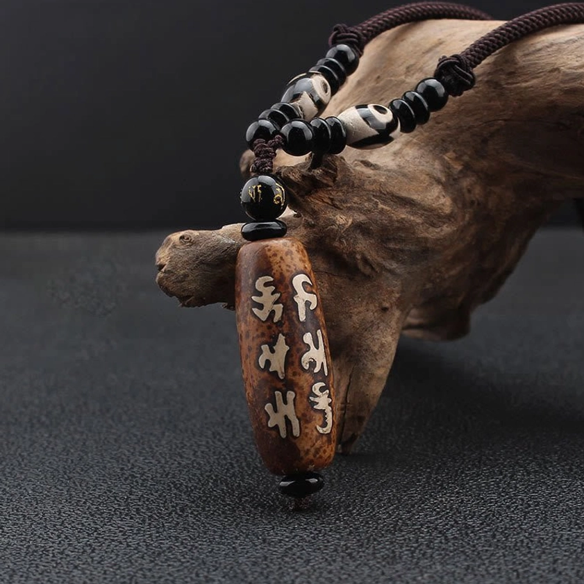 Side angle view of Buddhist Dzi bead pendant showing detailed Sanskrit carving and braided rope cord