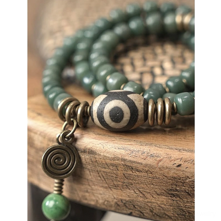 Macro close-up of dzi bead bracelet charm featuring three-eye symbol, bronze spacers, and green pendant