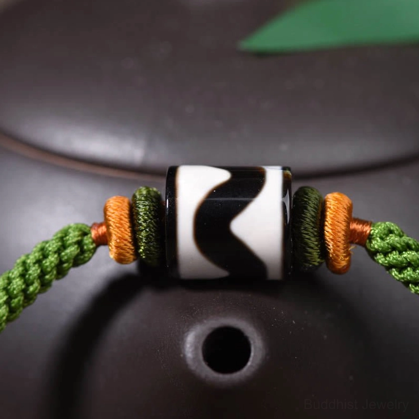 Close-up macro view of nine-eye dzi bead showing hand-painted black-white zigzag pattern and braided rope detail