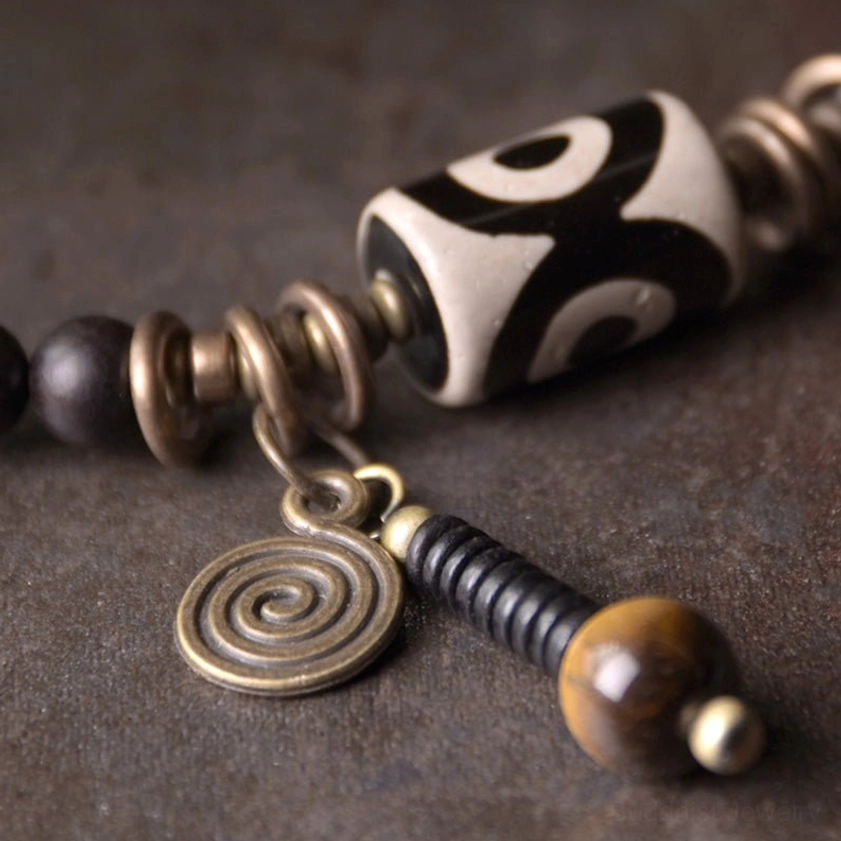 Detailed close-up of dzi bead with spiral metal charm and tiger eye accent showing hand-painted agate pattern
