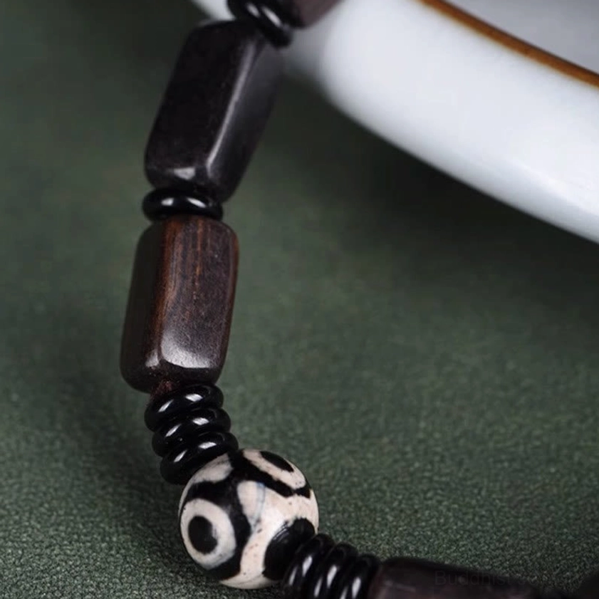 Extreme close-up macro shot of two-eye Dzi bead and ebony wood beads showing hand-painted details and natural wood grain