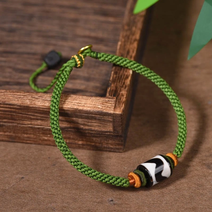 Handmade dzi bead bracelet side-top view on wooden tray, displaying green woven rope and protective agate stone detail