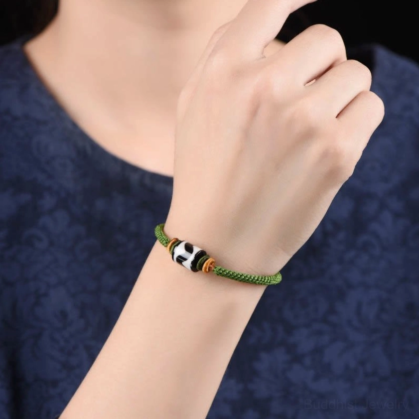 On-body wearing view of green rope dzi bead bracelet on wrist with dark blue clothing background