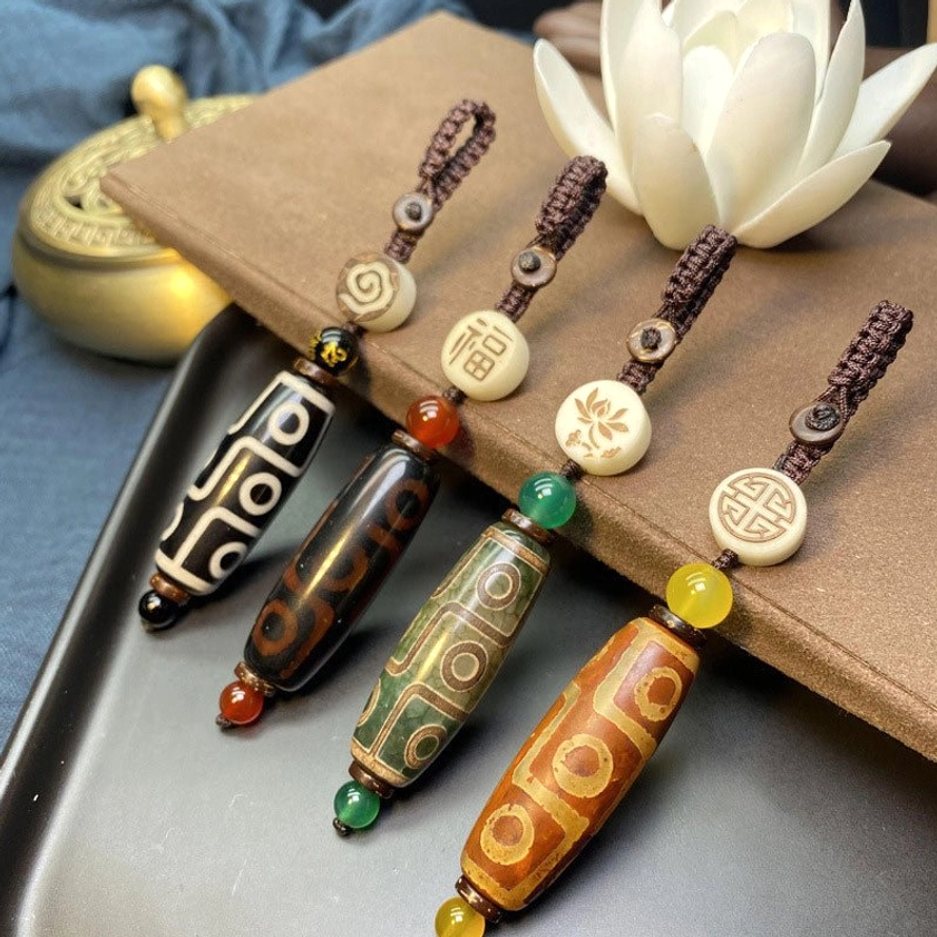 Assorted nine-eye dzi bead keychains in four distinct Buddhist styles displayed on tray with brown mat and white lotus decoration symbolizing spiritual significance