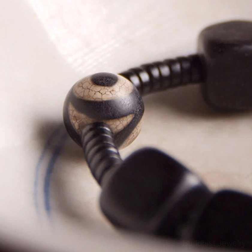 Close-up macro view of nine-eye dzi bead and dark wooden beads showing hand-painted spiritual charm details