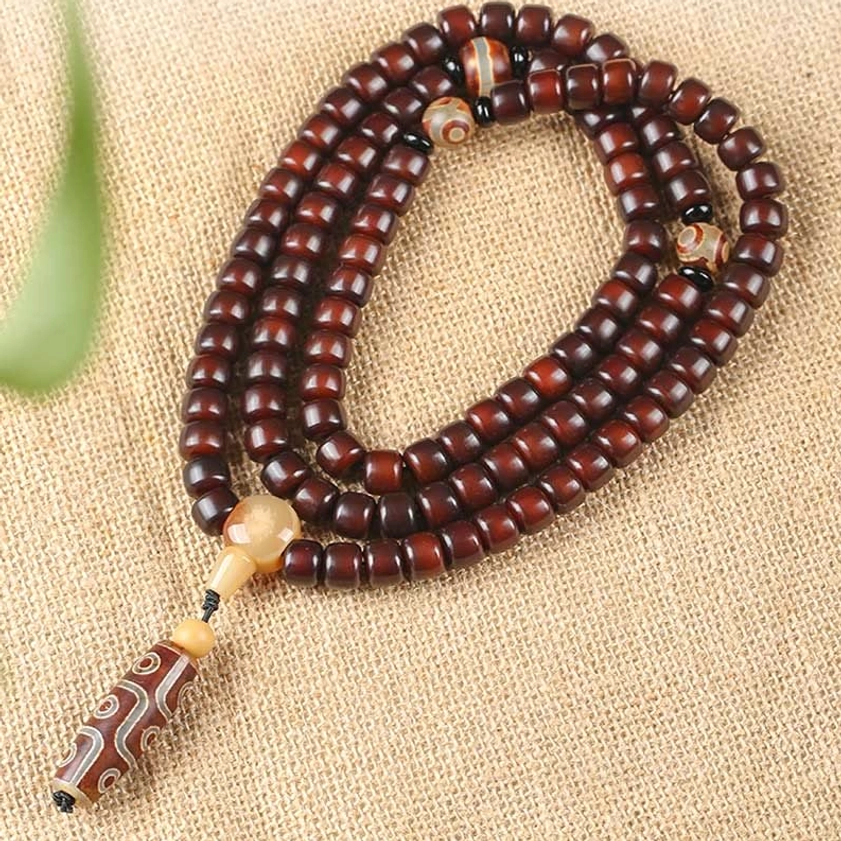 Looped Buddhist dzi bead mala necklace with three-eye pendant, jade spacers, and natural stone beads displayed with green leaf for spiritual meditation tool