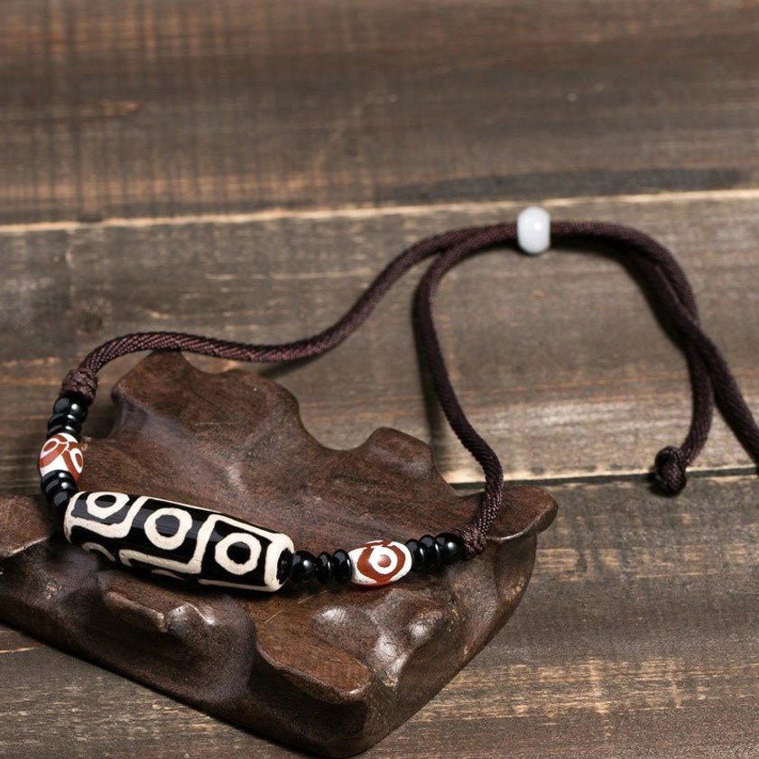 Buddhist dzi bead protection necklace with black-white pattern, adjustable brown cord with toggle clasp, displayed on wooden stand