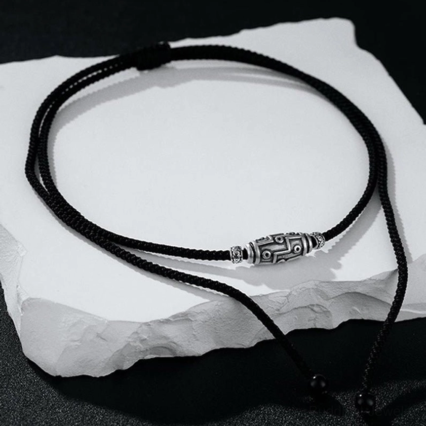 Buddhist dzi necklace top-down view with adjustable sliding knot on black background with stone display prop