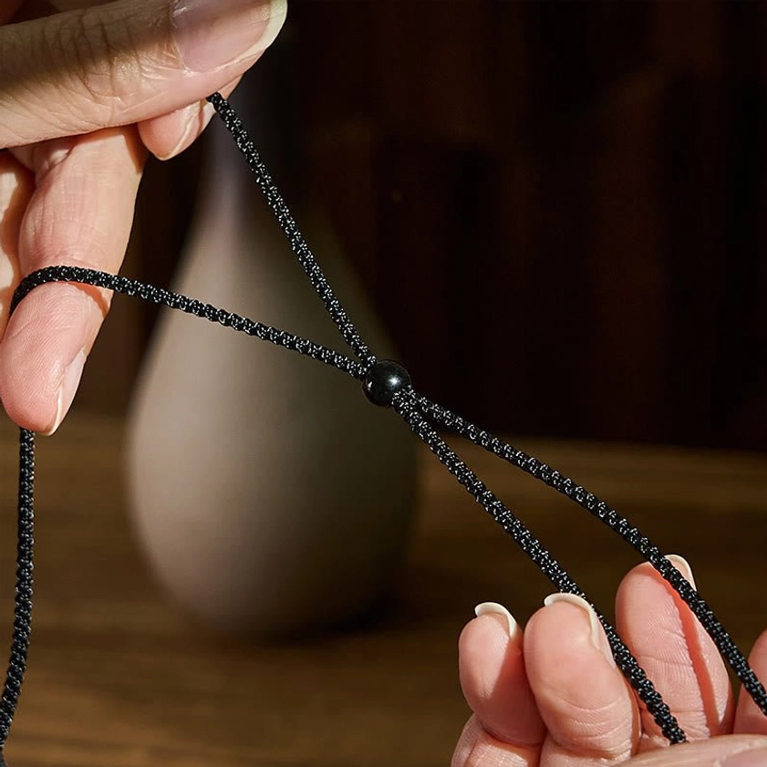Hand-held nine-eye dzi bead necklace showing detailed braided cord texture and black sliding adjuster bead