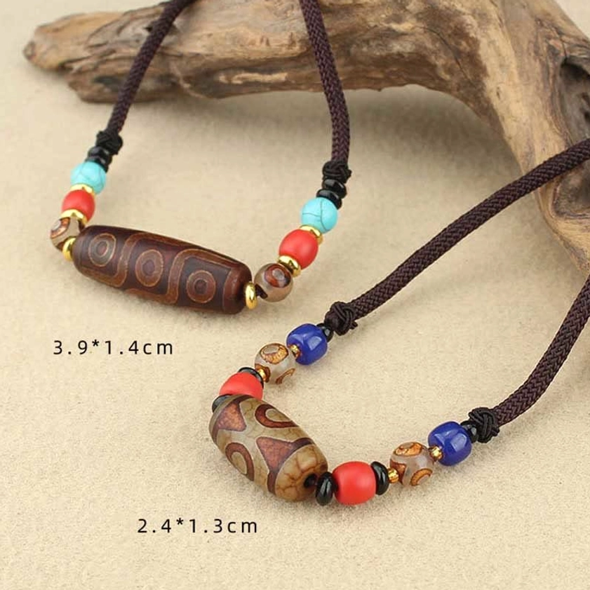 Close-up comparison of nine-eye dzi bead and three-eye dzi bead Buddhist pendants with color-matched spacer beads on wooden background
