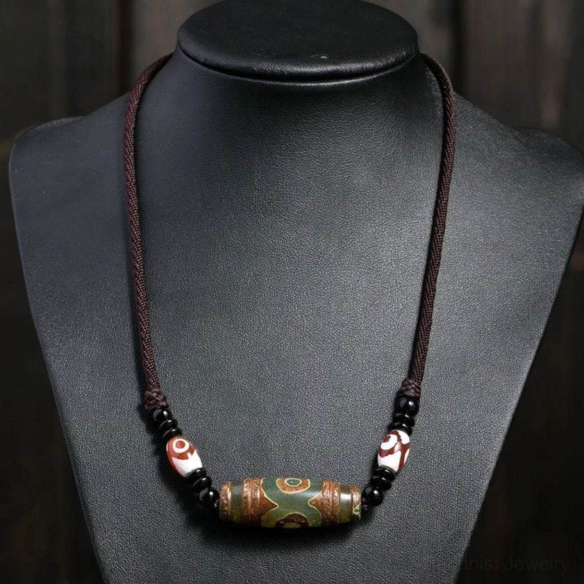 Green dzi bead Buddhist amulet necklace worn on jewelry mannequin, brown braided cord with matching spacer beads, front view